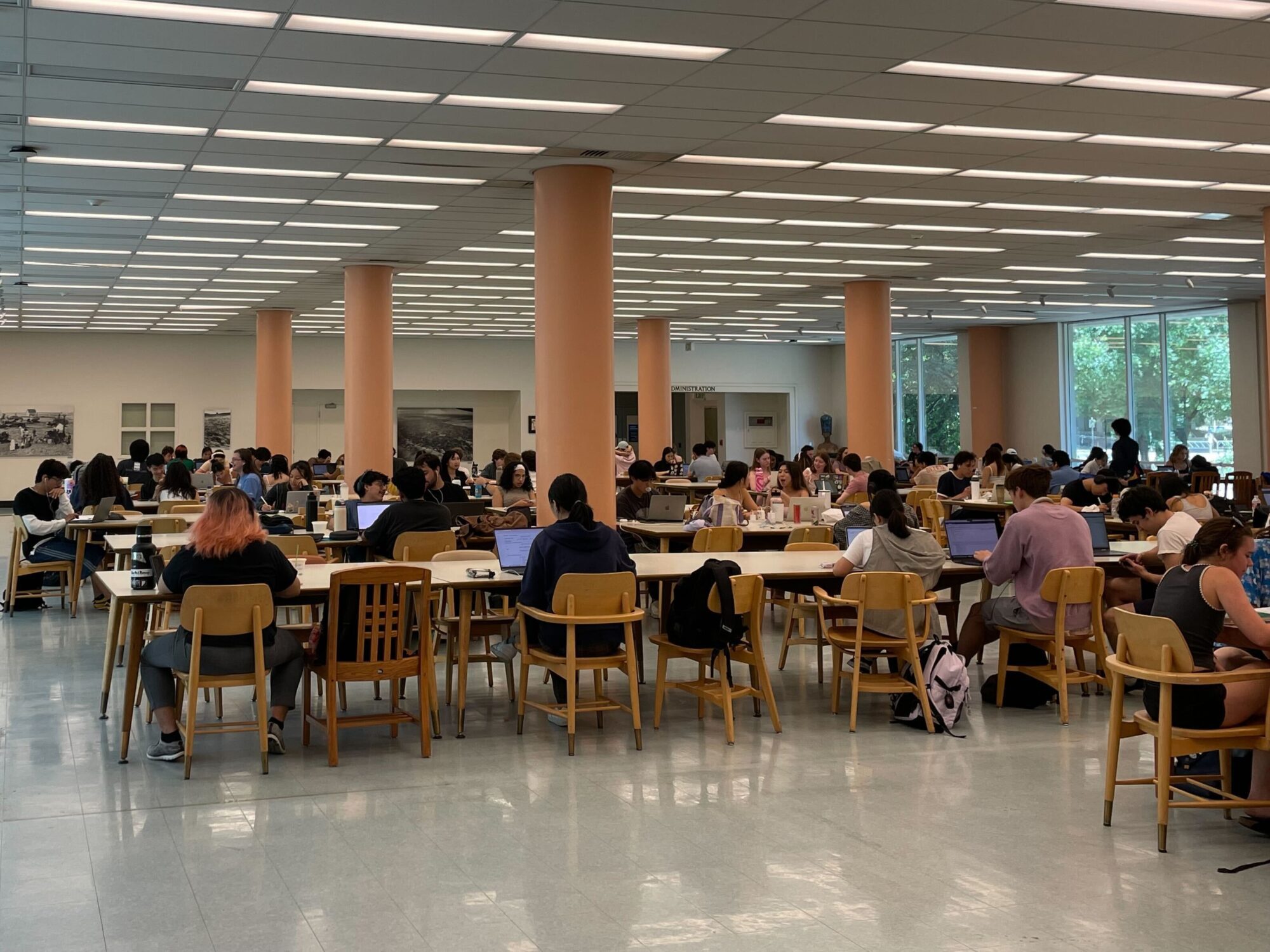 Study tables filled with students. Trees are visible through the large windows in the background.