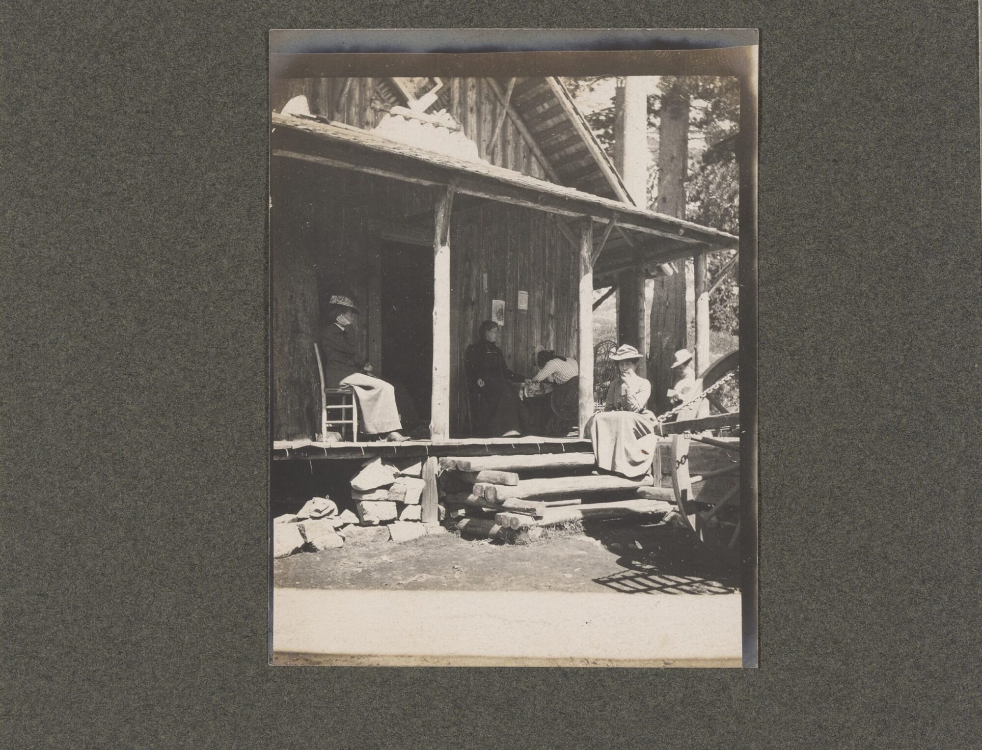 A black and white photograph of various women sitting outside a cabin.