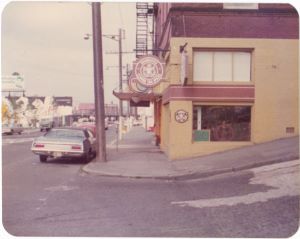 An old photograph of an old yellow-painted Starbucks store with a orange-brown sign on the corner of a block with several cars outside.