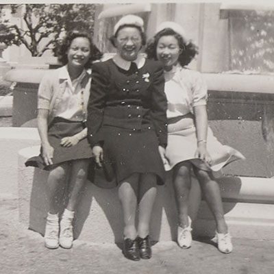 A black and white photograph of three girls sitting on a concrete bench.