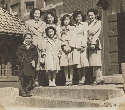 A black and white photograph of a group of women and girls standing on a doorstep in midcentury clothing.