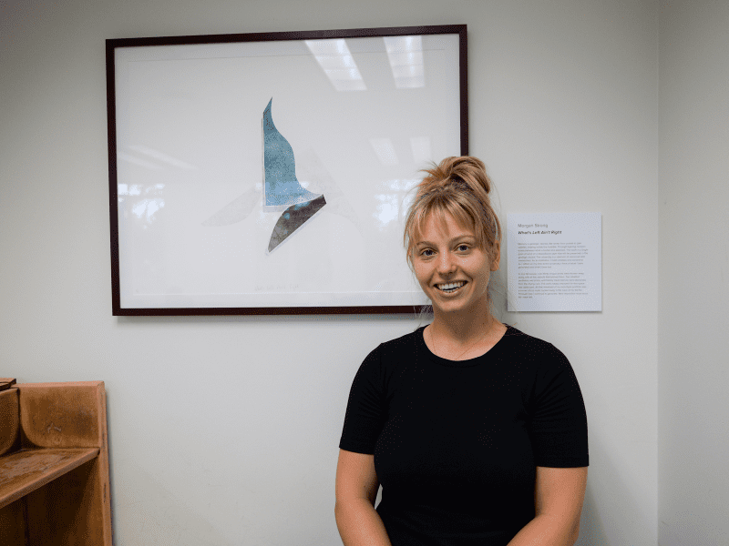 Student Morgan Strong poses in front of framed art with blue, black and white wing-like shapes on white background.