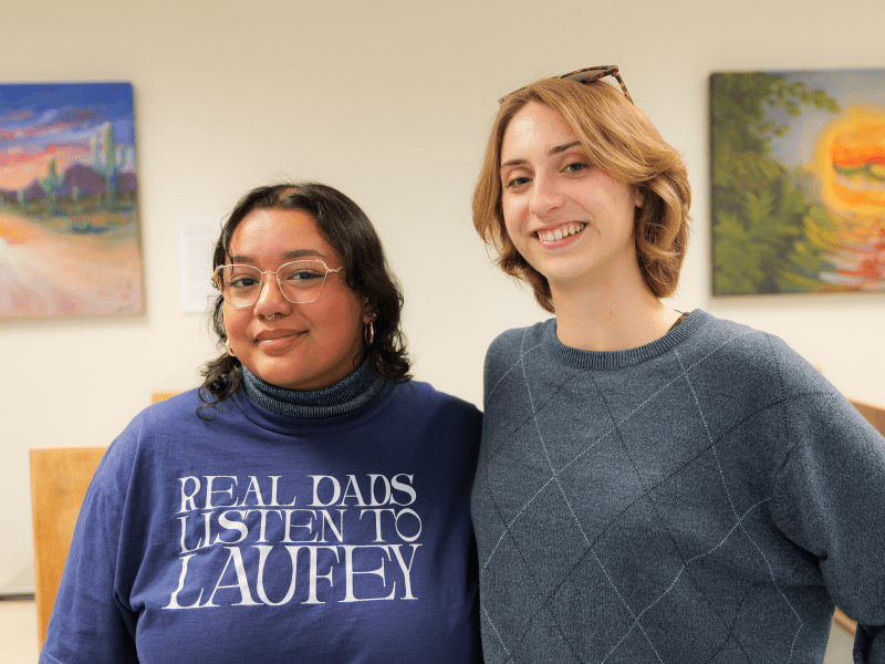 Emily Gavidia and Madison Seeman pose in front of student artwork in the 24-Hour Study Room at Shields Library