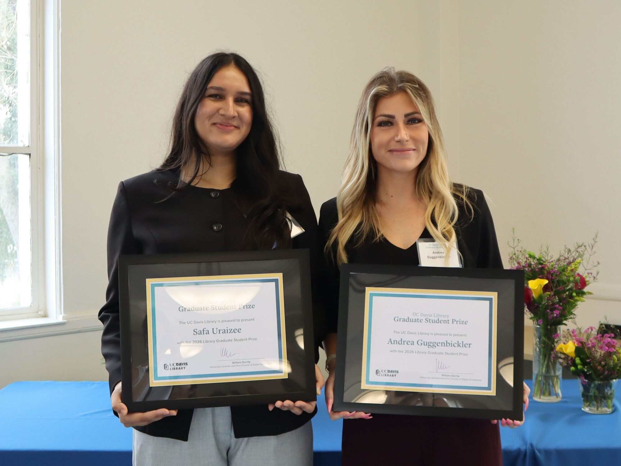 Two female graduate students holding framed prize certificates.