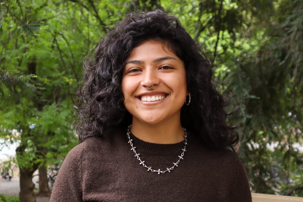 Portrait of Camila Cancino with green tree branches in the background.