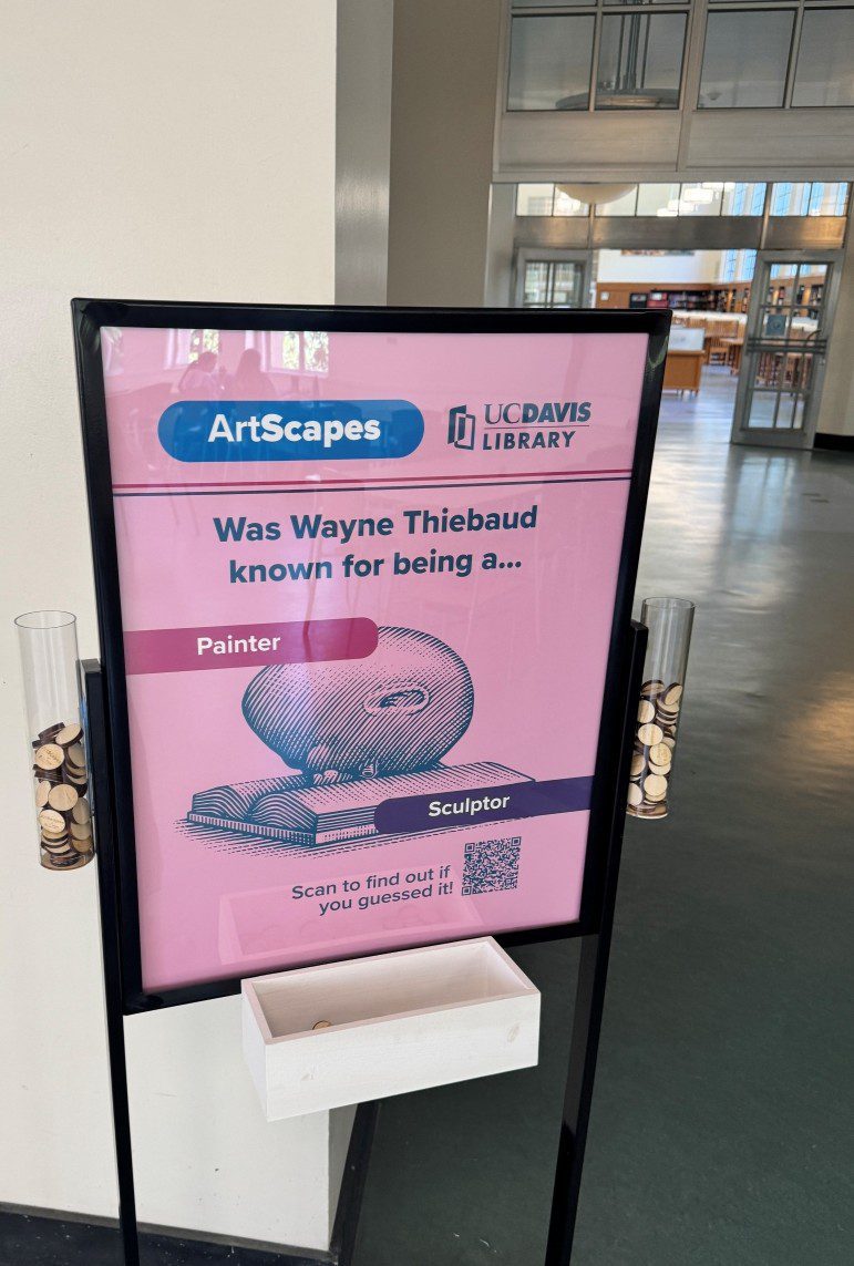 A framed pink poster reads: ArtScapes -- Was Wayne Thiebaud known for being a painter or sculptor? Wooden coins dropped in glass tubes on each side of the poster represent a fairly even split between those two choices.